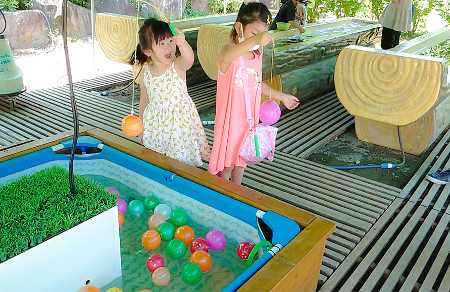 ハーブ庭園の夏イベントで、プールに浮かぶ色鮮やかな水風船のヨーヨーすくいを笑顔で楽しむ2人の女の子。